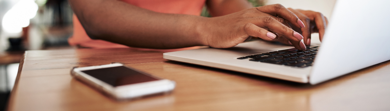 Hands typing on laptop with phone on table